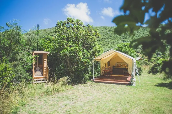 Ein Glamping-Zelt aus Canvas und ein hölzernes Toilettenhäuschen auf einer Grasfläche.