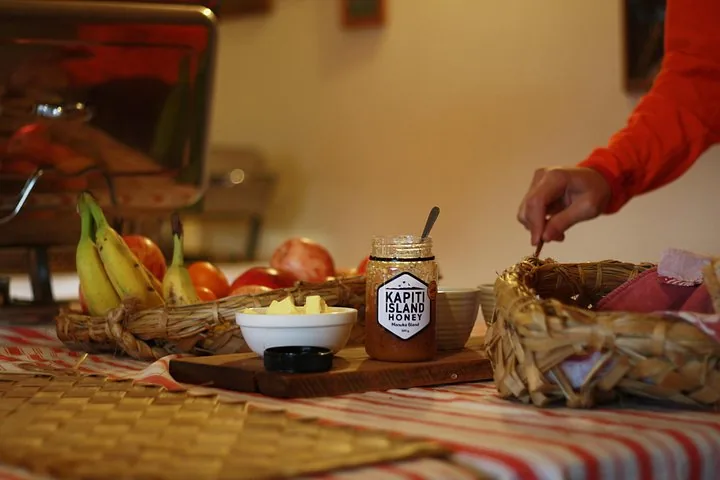 Un frasco de miel de manuka de la isla Kapiti sobre una mesa con fruta y pan.