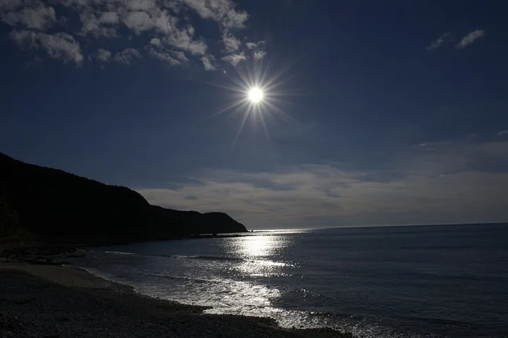 The sun reflecting on the ocean next to a dark coastline silhouette.
